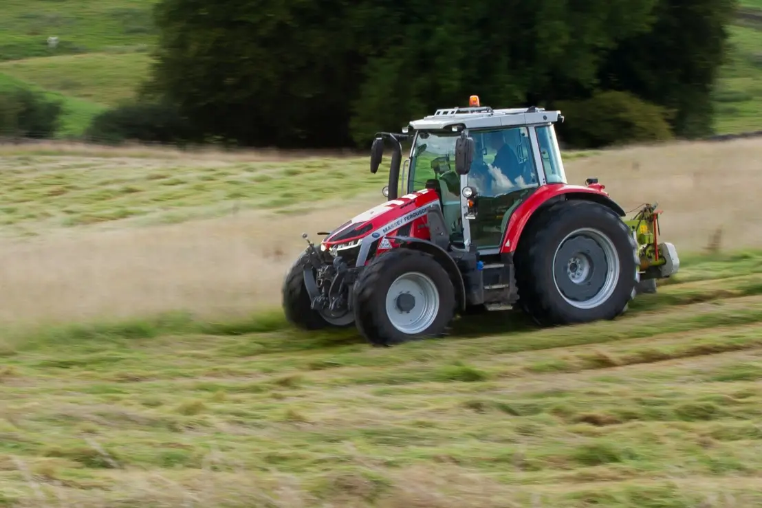 Traktor se žacím strojem při sečení vysoké trávy na louce